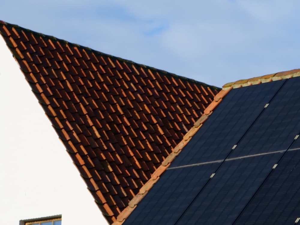 Photovoltaikmodule auf einem Ziegeldach vor hellem Himmel.