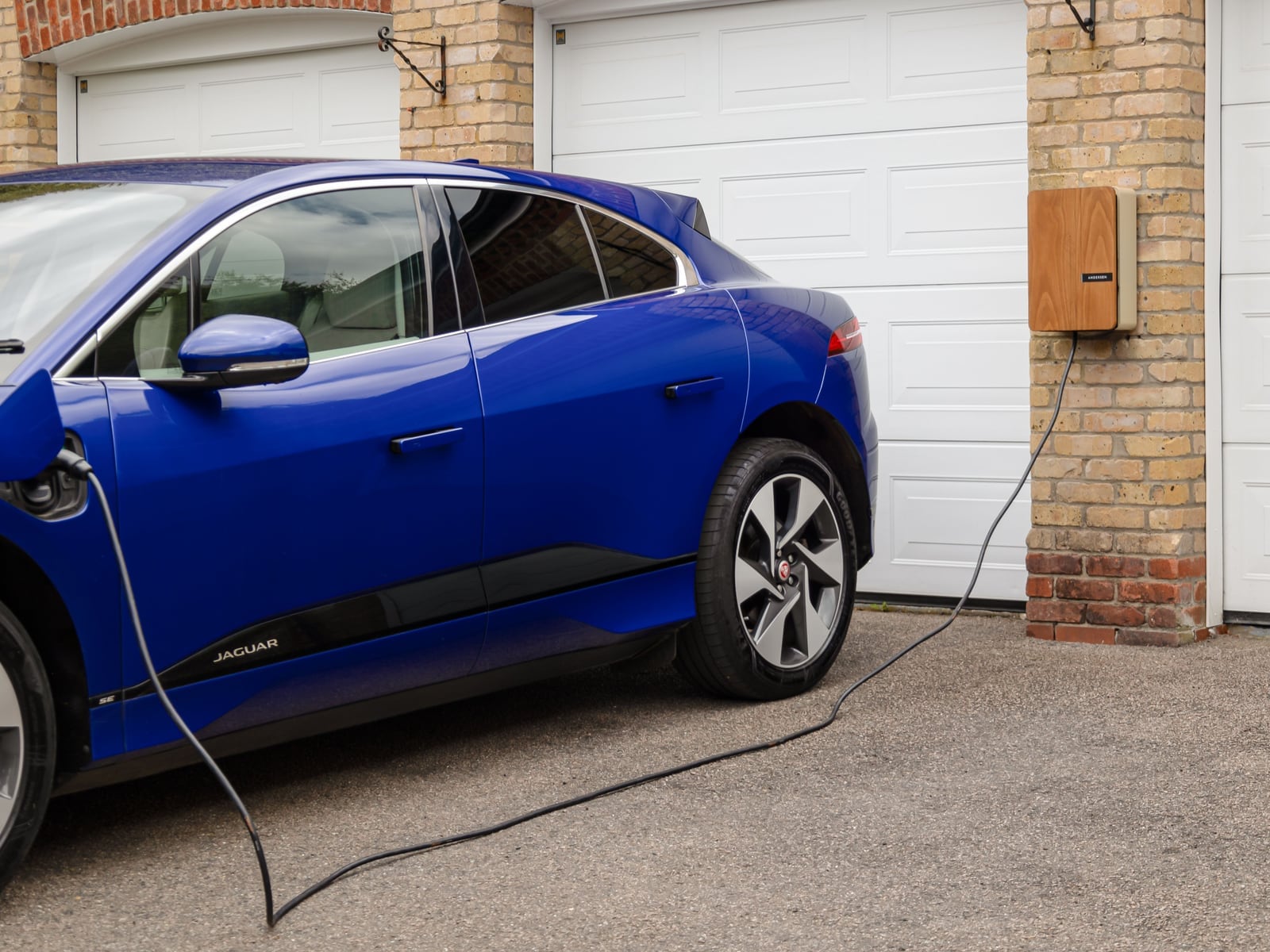 Elektroauto an einer Wandladestation vor einer Garage.